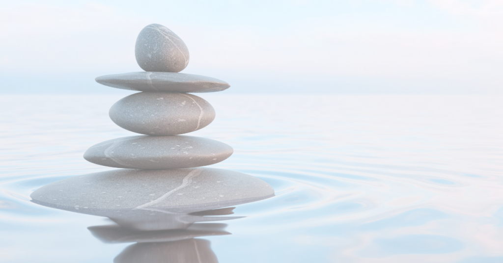 Balancing stones on a light blue body of water.